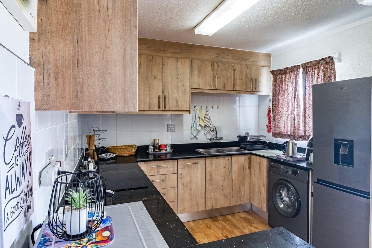 A functional kitchen featuring wood-look laminate cabinetry, black granite countertops, a double bowl sink, and an integrated washing machine.