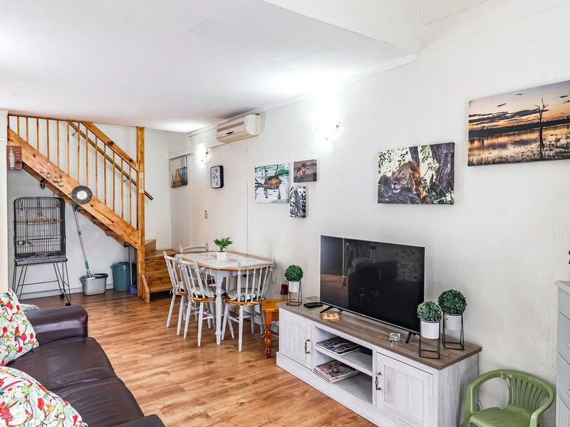 Open-plan living and dining area featuring laminate flooring, a wooden staircase, and a wall-mounted air conditioning unit.