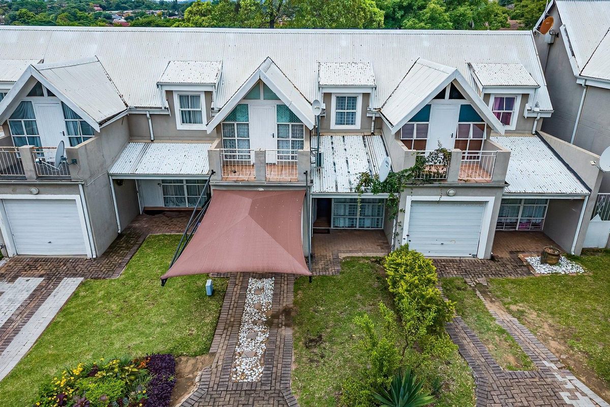 Aerial view of a townhouse complex featuring corrugated metal roofing, private balconies, garage access, and established garden areas with paved pathways.