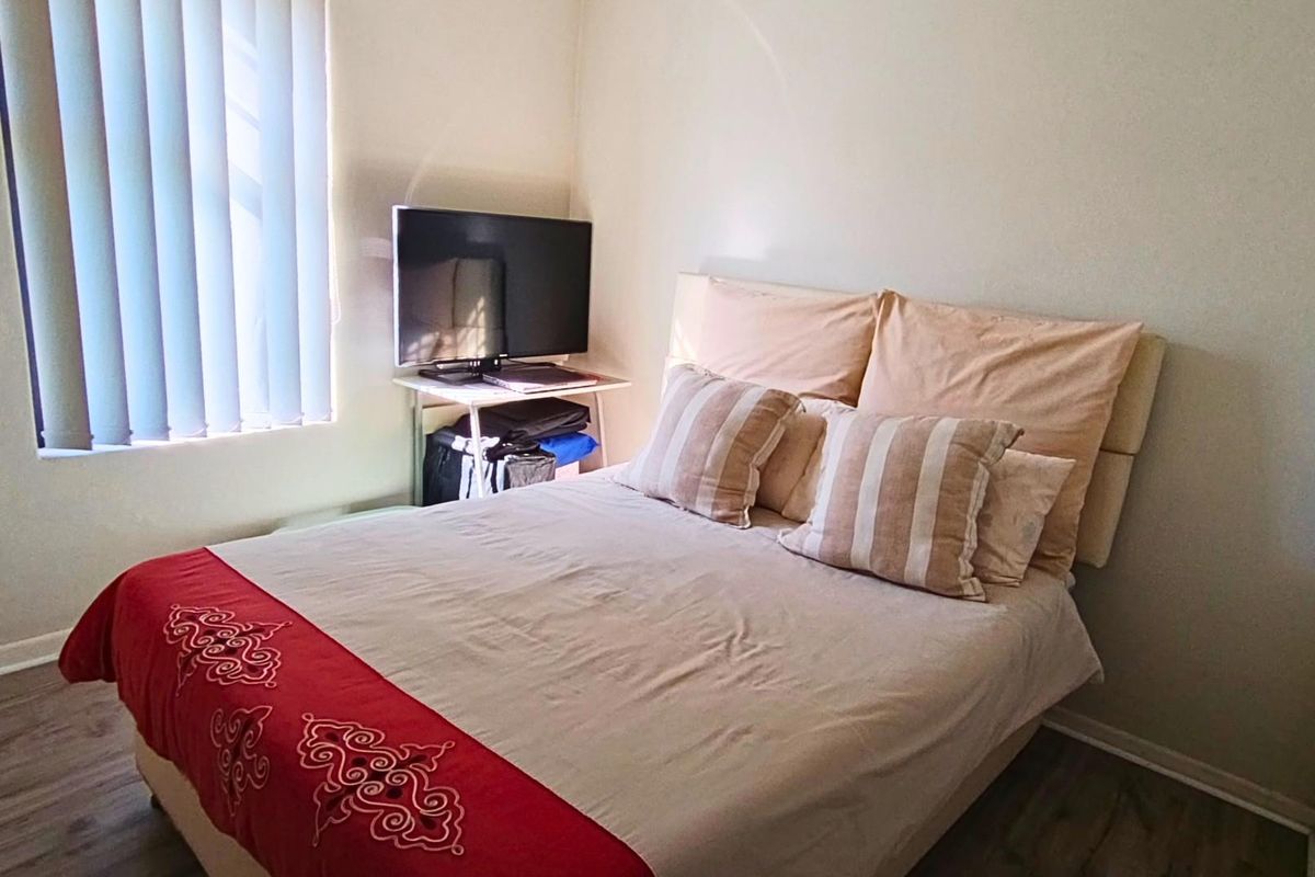A functional bedroom featuring laminate flooring and vertical blinds, providing a neutral base for personalization.