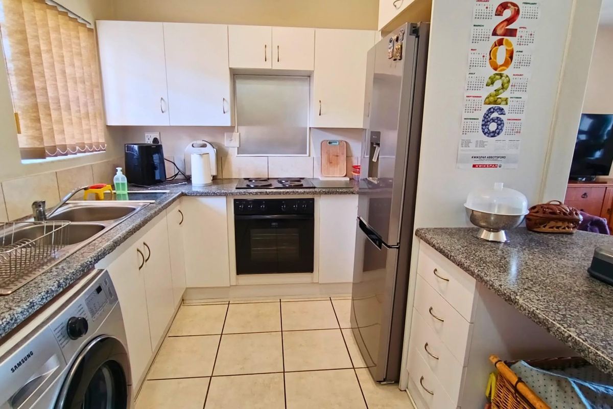 Functional kitchen featuring white cabinetry, granite countertops, built-in oven and hob, double basin sink, and tiled flooring with space for a washing machine.