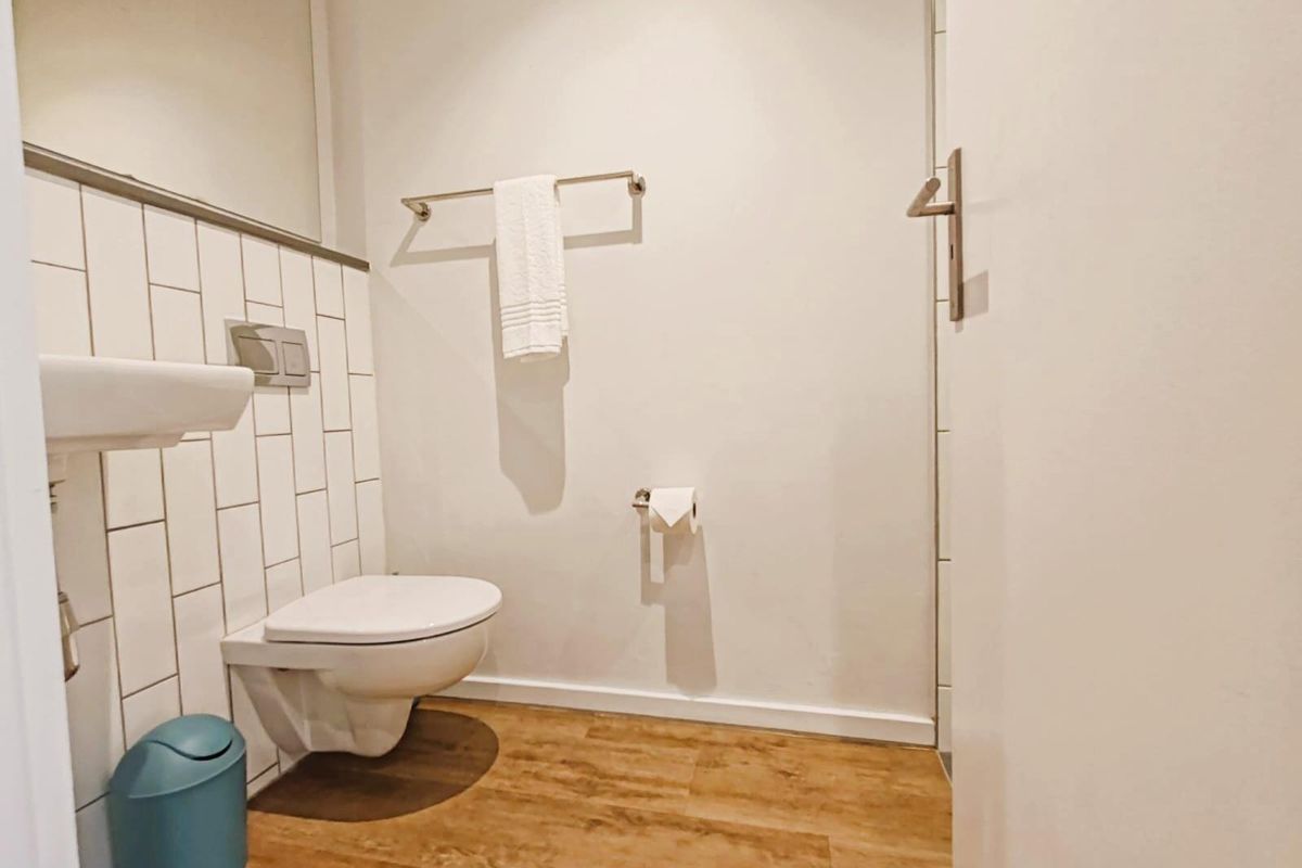 A modern bathroom featuring a wall-mounted toilet, a sleek basin, and stylish subway-style wall tiling with wood-look flooring.