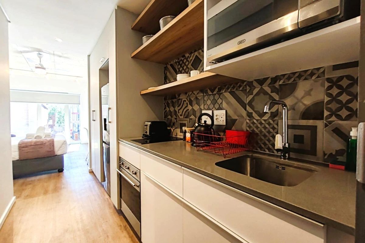 Modern galley-style kitchen featuring stone countertops, built-in oven, hob, extractor fan, and decorative tiled backsplash with open shelving.