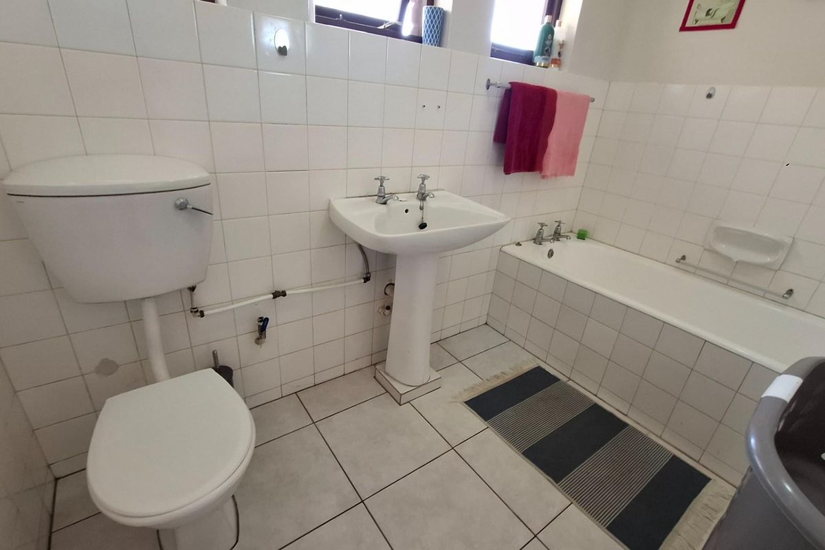 A functional bathroom featuring a pedestal basin, toilet, and bathtub with white wall tiling and tiled flooring.