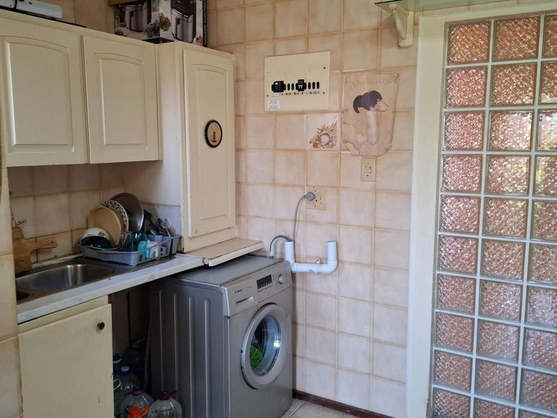 A functional laundry area featuring built-in cabinetry, a stainless steel sink, and a distinctive glass block wall, requiring cosmetic updates to modernize the space.