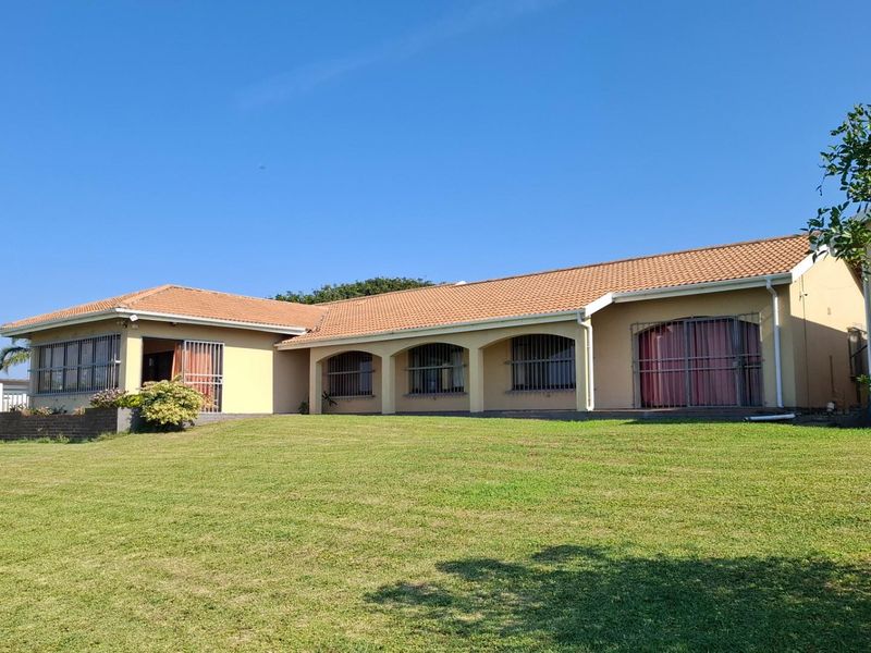 Rear view of a single-story house featuring a large lawn, terracotta tiled roof, and arched patio openings with security bars.