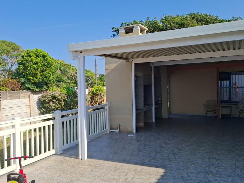 A spacious covered patio featuring tiled flooring, a built-in braai, and a white balustrade, offering an ideal space for outdoor entertaining.