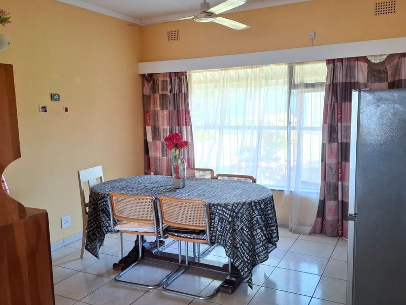 A functional dining area featuring tiled flooring, a ceiling fan, and a large window that allows for natural light.