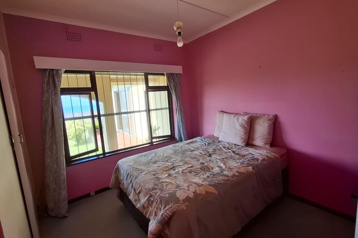 A bedroom featuring pink walls, built-in cupboards, and security bars on the windows, offering a functional space ready for cosmetic updates.