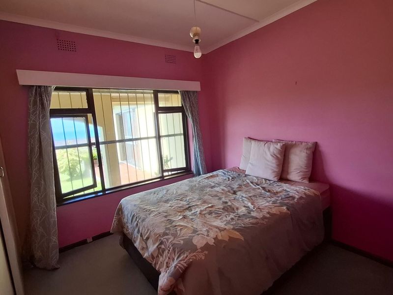 A bedroom featuring pink walls, built-in cupboards, and security bars on the windows, offering a functional space ready for cosmetic updates.