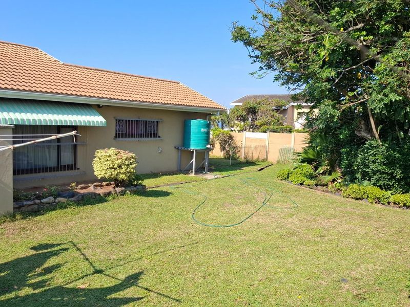 Rear view of the property featuring a lawned garden, boundary wall, and a water storage tank attached to the exterior wall.