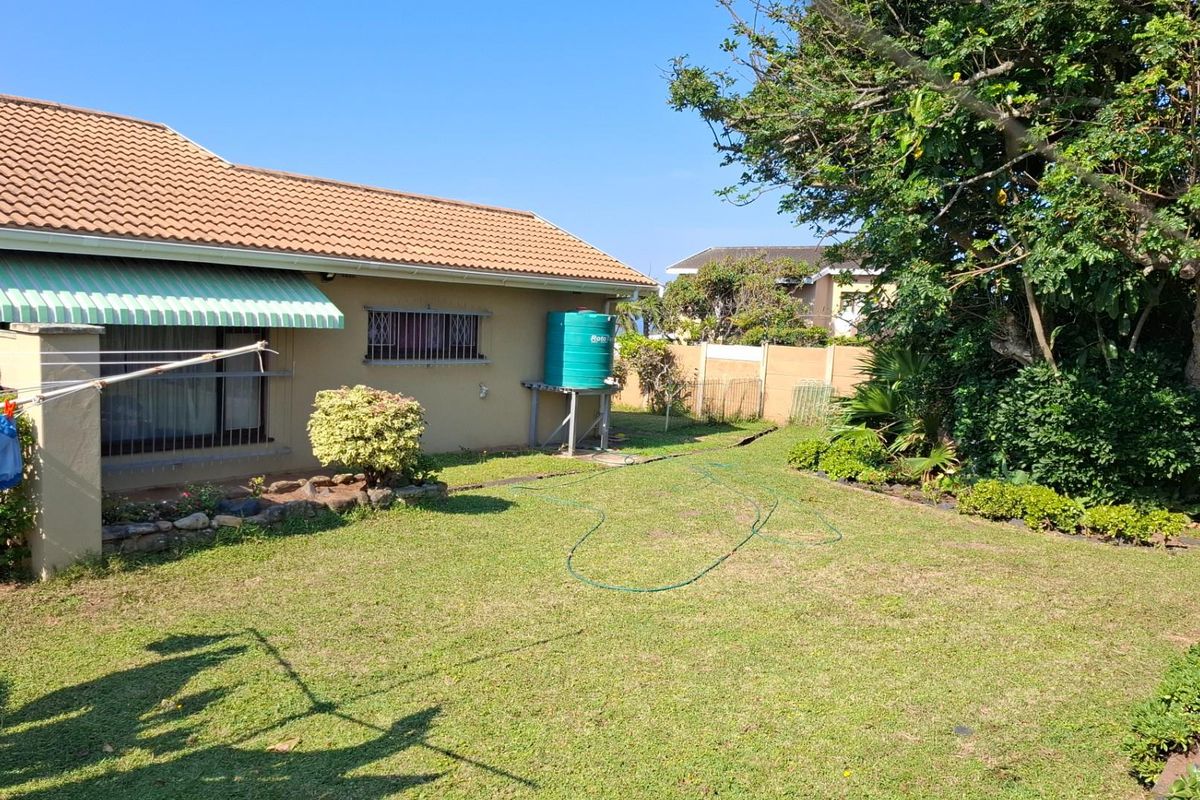 Rear view of the property featuring a lawned garden, boundary wall, and a water storage tank attached to the exterior wall.