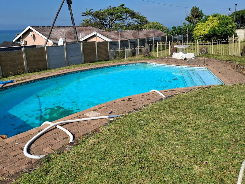 Outdoor swimming pool area featuring paved surround, metal perimeter fencing, and views of the surrounding neighborhood and coastline.