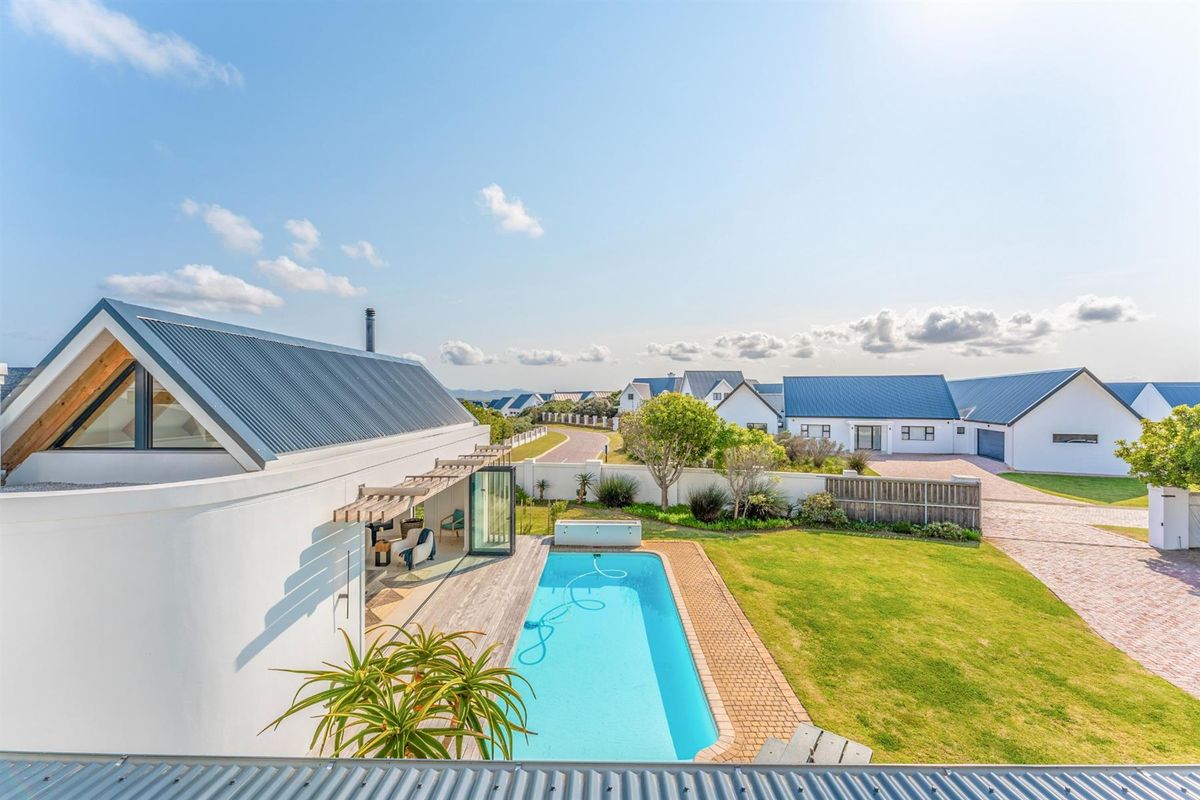 Elevated view of a modern residence featuring a swimming pool, timber decking, landscaped garden, and paved driveway within a secure estate.