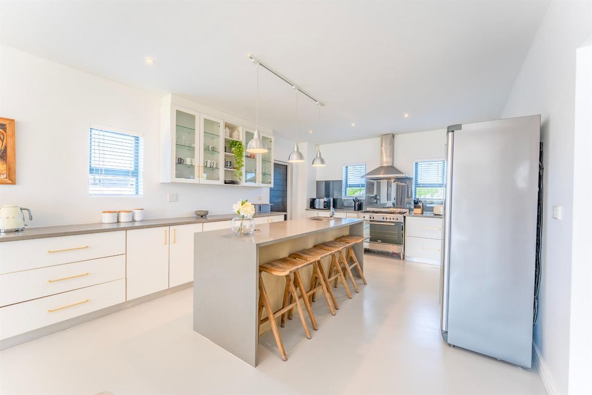Modern kitchen featuring a central island with breakfast bar seating, sleek cabinetry, stainless steel range cooker, and integrated extractor fan.