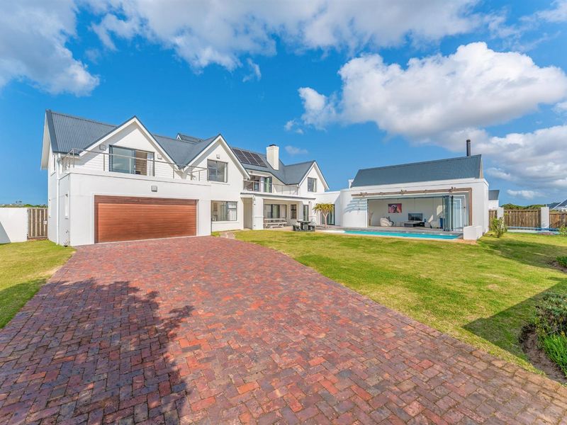A spacious modern residence featuring a brick driveway, manicured lawn, swimming pool, and a detached structure with large glass doors opening to the garden.