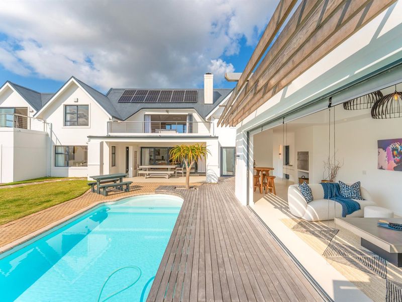 A spacious rear exterior view featuring a swimming pool, timber decking, covered patio, and a modern two-story residence with solar panels.