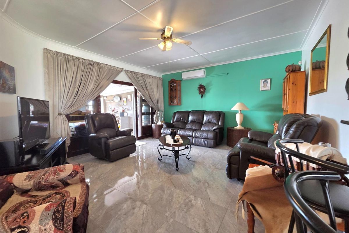A spacious living room featuring tiled flooring, a ceiling fan, and a wall-mounted air conditioning unit, with direct access to an adjoining space.