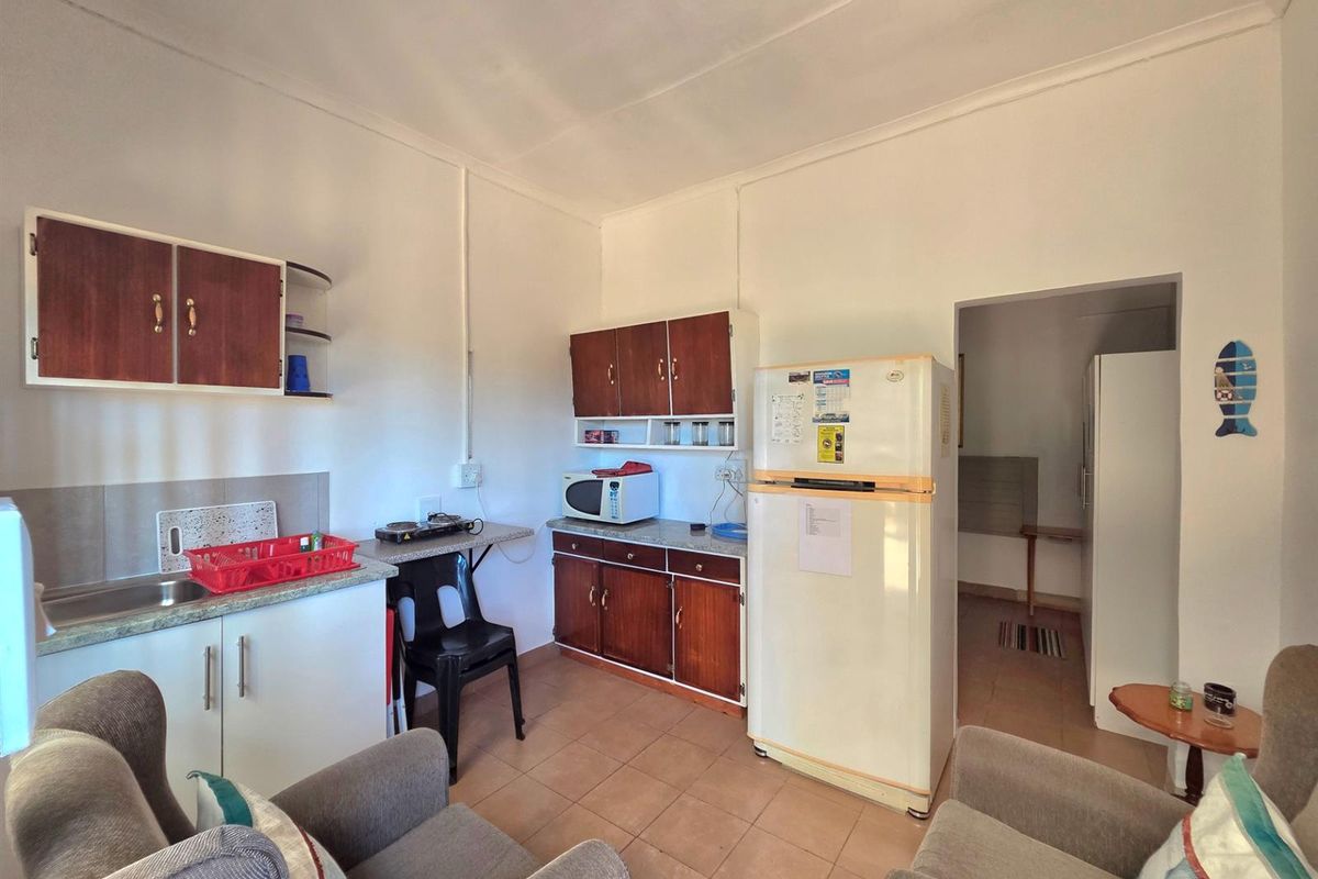 A compact, dated kitchen featuring laminate cabinetry, stone-look countertops, and tiled flooring, with an adjacent utility area visible through the doorway.