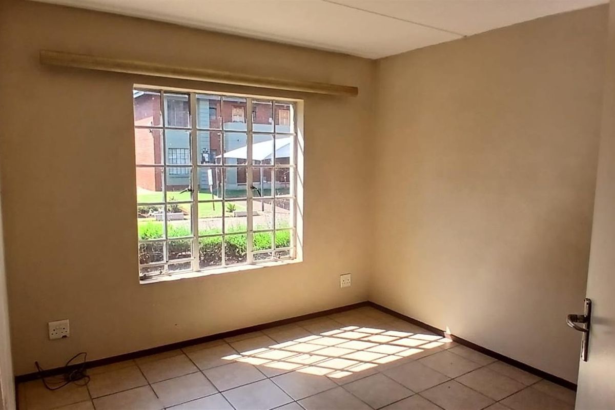 A vacant bedroom featuring tiled flooring, neutral wall paint, and a metal-framed window overlooking the complex grounds.