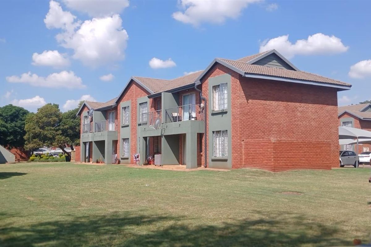 Exterior view of a multi-story brick apartment complex featuring balconies and a shared lawn area.