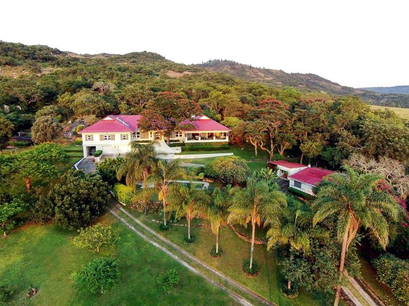 Aerial view of a sprawling farm property featuring a main residence with a red metal roof, secondary outbuildings, and extensive landscaped grounds.