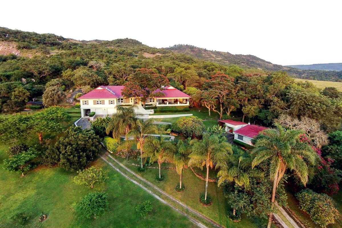 Aerial view of a sprawling farm property featuring a main residence with a red metal roof, secondary outbuildings, and extensive landscaped grounds.