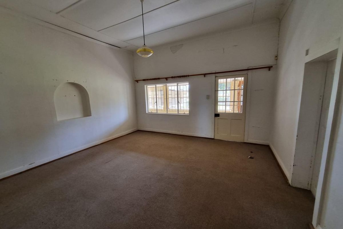 An empty living room featuring an arched wall niche, timber-framed windows, and a glass-paneled door, requiring cosmetic updates to restore its appeal.