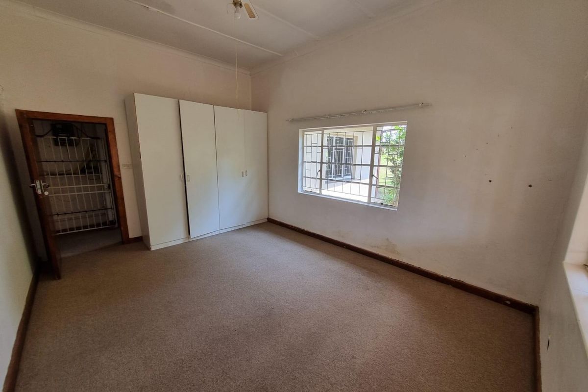 A vacant bedroom featuring built-in cupboards, carpeted flooring, and security bars on the window, offering a blank canvas for renovation.