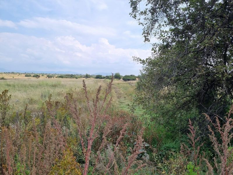 A scenic view of the expansive open farm landscape featuring natural vegetation and distant hills under a cloudy sky.