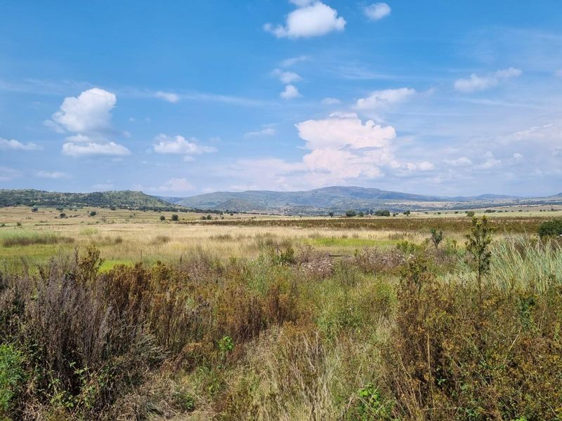 A scenic view of the expansive farm landscape featuring rolling fields and distant mountain ranges under a clear blue sky.