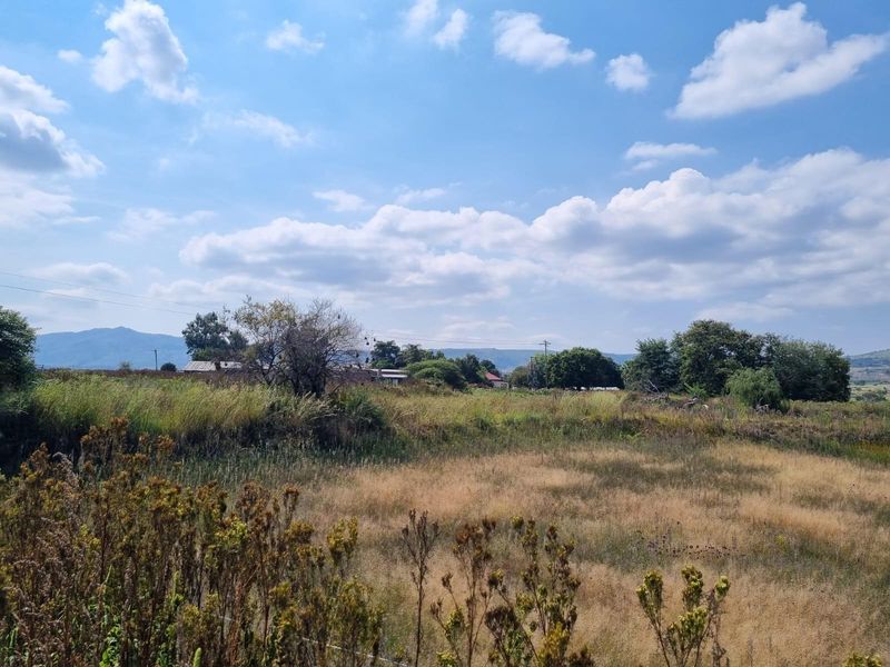 A scenic view of the expansive farm landscape featuring open fields, natural vegetation, and distant mountain ranges under a clear blue sky.