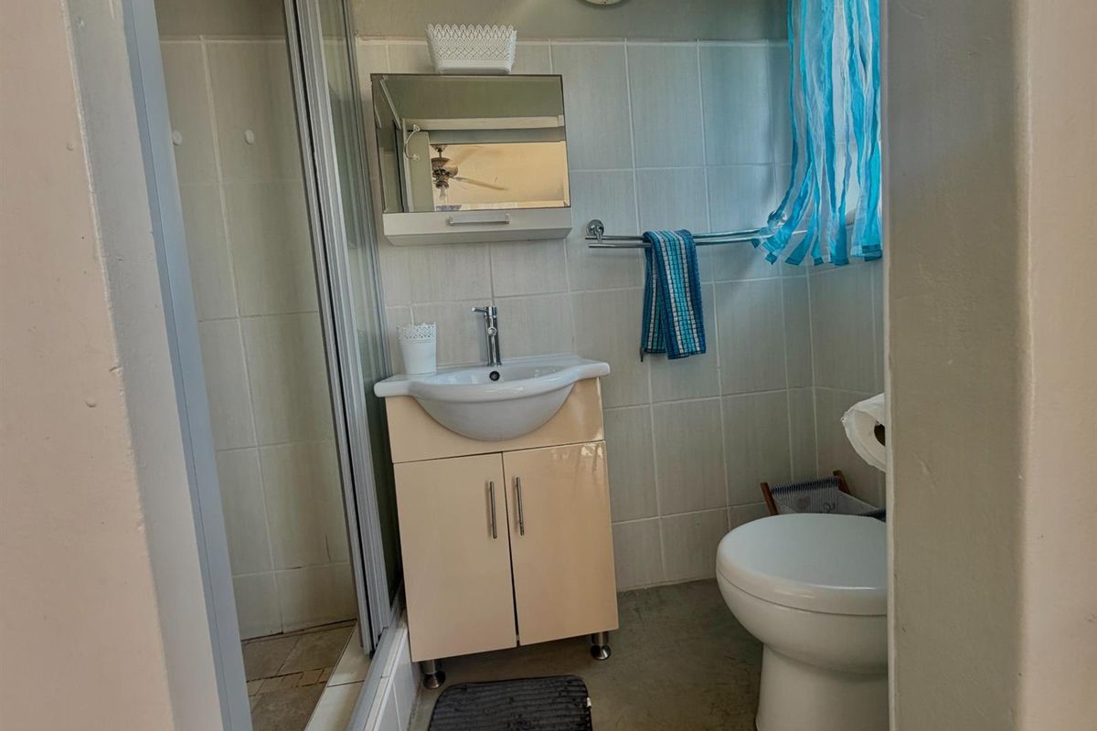 A compact bathroom featuring a shower enclosure, a vanity basin with storage, and a standard toilet, finished with wall tiles.