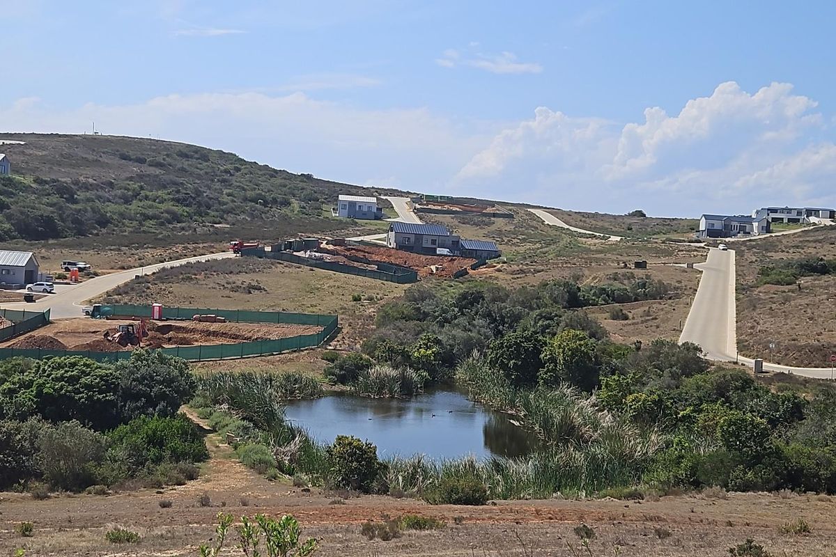 An elevated view of a residential development site featuring a natural pond, surrounding vegetation, paved roads, and ongoing construction of residential properties.