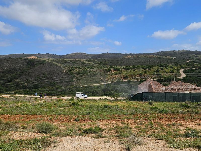 A wide-angle view of a vacant residential plot featuring natural landscape and an ongoing construction project in the background.