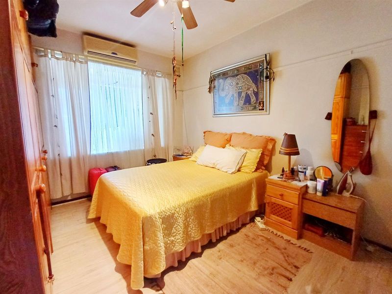 A functional bedroom featuring a ceiling fan, wall-mounted air conditioning unit, and built-in wardrobe storage.
