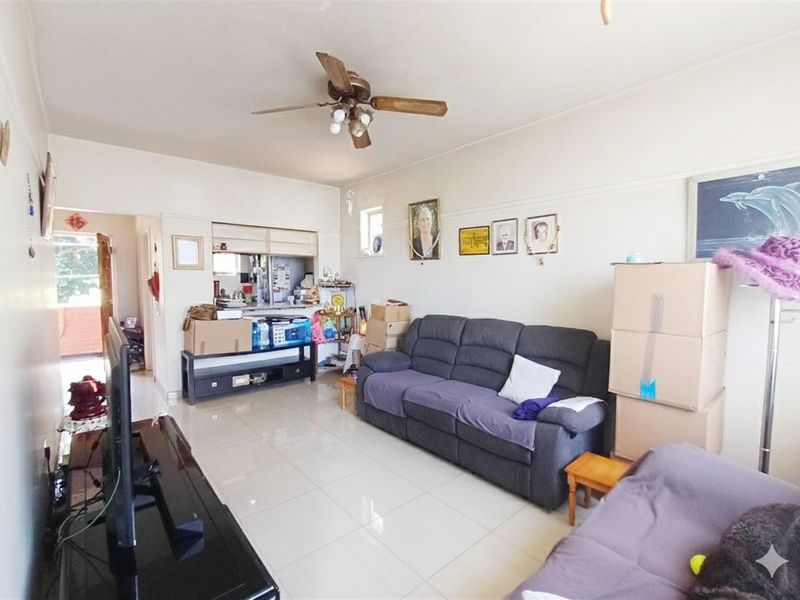 A living room featuring tiled flooring, a ceiling fan, and a convenient pass-through window connecting to the kitchen area.