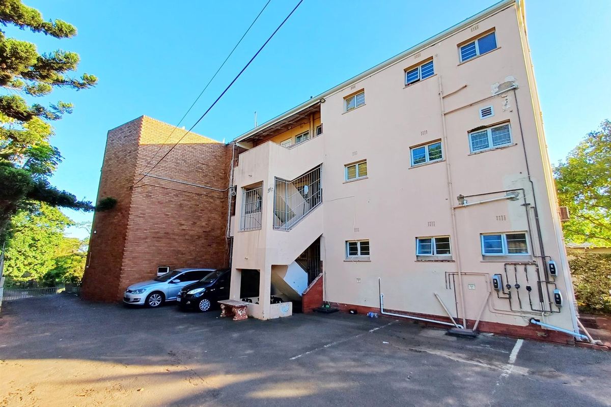 Rear elevation of a multi-story apartment building featuring an external staircase, exposed brick section, and paved parking area.