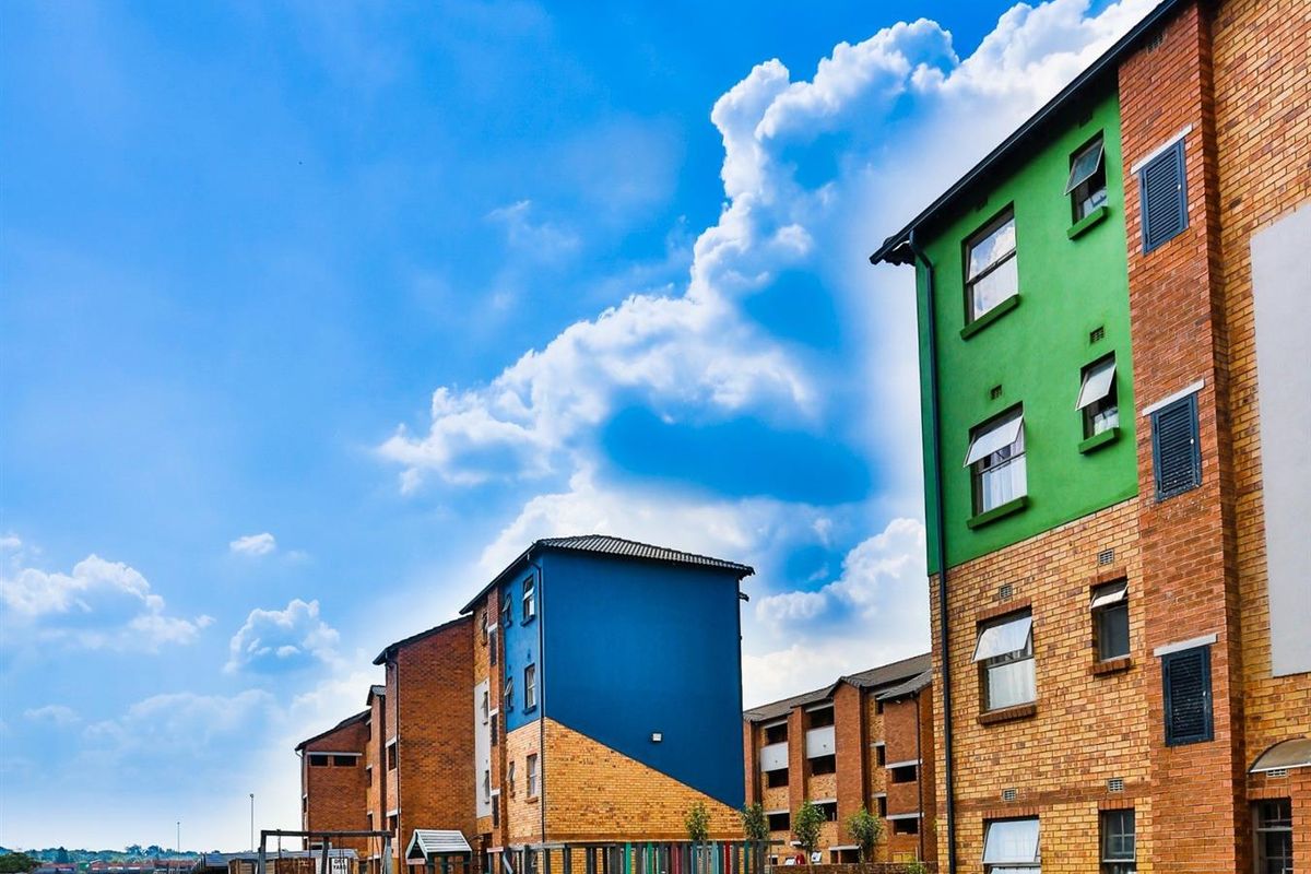 Exterior view of a multi-story apartment complex featuring colorful brick facades, casement windows, and a communal playground area set within a landscaped garden.