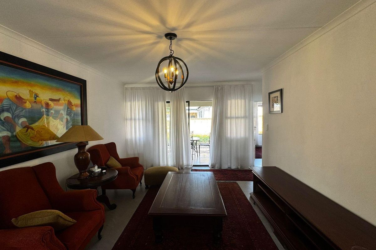 A comfortable living room featuring a central pendant light, cove cornicing, and a sliding glass door providing access to the outdoor patio area.