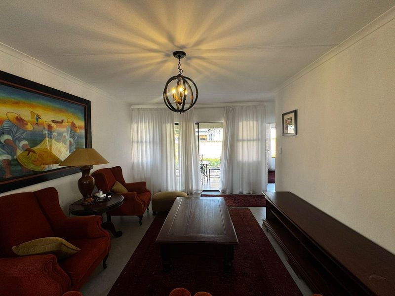 A comfortable living room featuring a central pendant light, cove cornicing, and a sliding glass door providing access to the outdoor patio area.