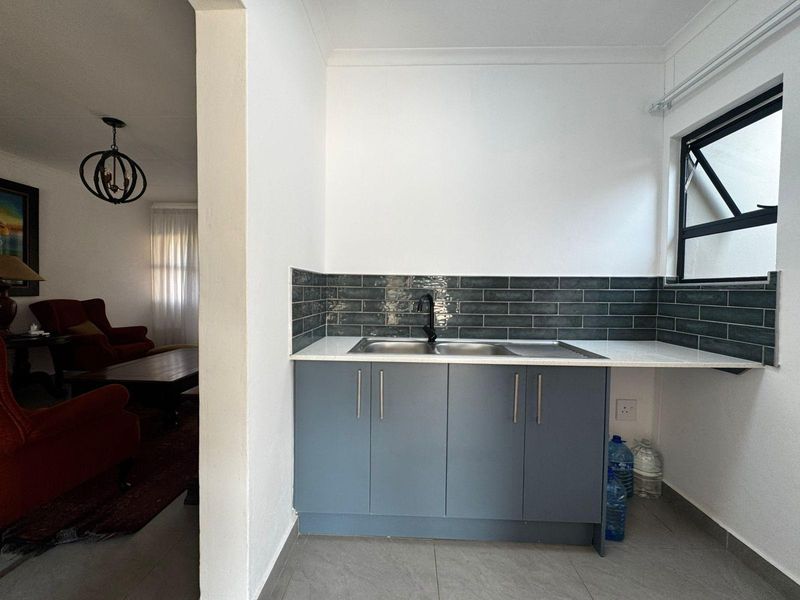 A clean and functional scullery area featuring modern grey cabinetry, a stainless steel sink, and a stylish dark subway tile backsplash.