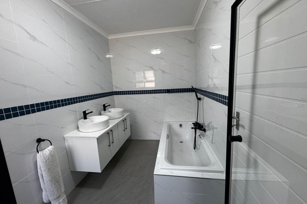 Modern bathroom featuring a double vanity with vessel sinks, a built-in bathtub with shower attachment, and contemporary marble-look wall tiling.