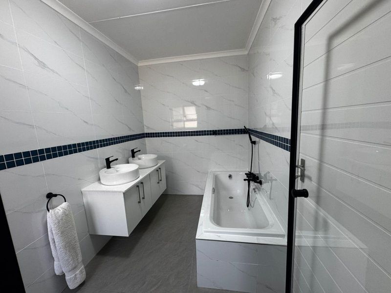 Modern bathroom featuring a double vanity with vessel sinks, a built-in bathtub with shower attachment, and contemporary marble-look wall tiling.