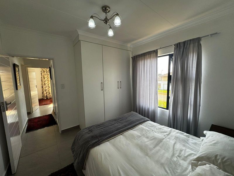 A well-maintained bedroom featuring built-in wardrobes, tiled flooring, and a ceiling light fixture, with a view through the window to the exterior.