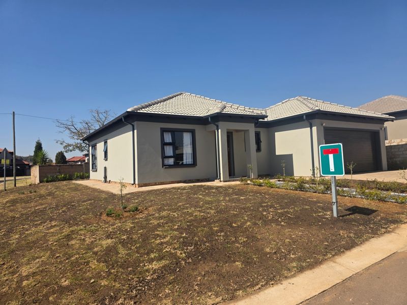 Modern single-story residential home featuring a tiled roof, double garage, and neutral exterior paint, situated on a corner plot with a developing garden.