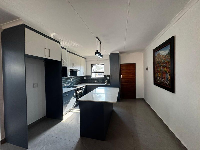 Modern kitchen featuring a central island, sleek two-tone cabinetry, stone countertops, tiled backsplash, and integrated appliances with contemporary pendant lighting.