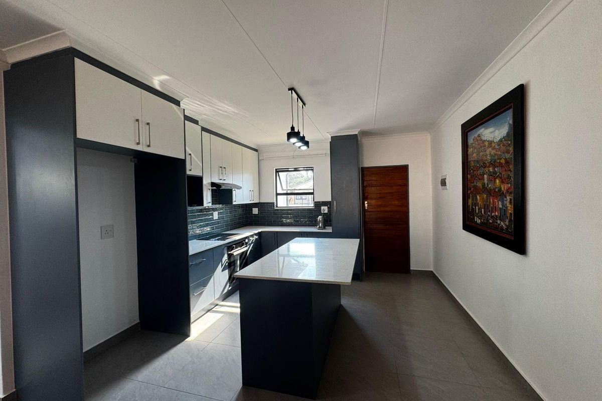 Modern kitchen featuring a central island, sleek two-tone cabinetry, stone countertops, tiled backsplash, and integrated appliances with contemporary pendant lighting.