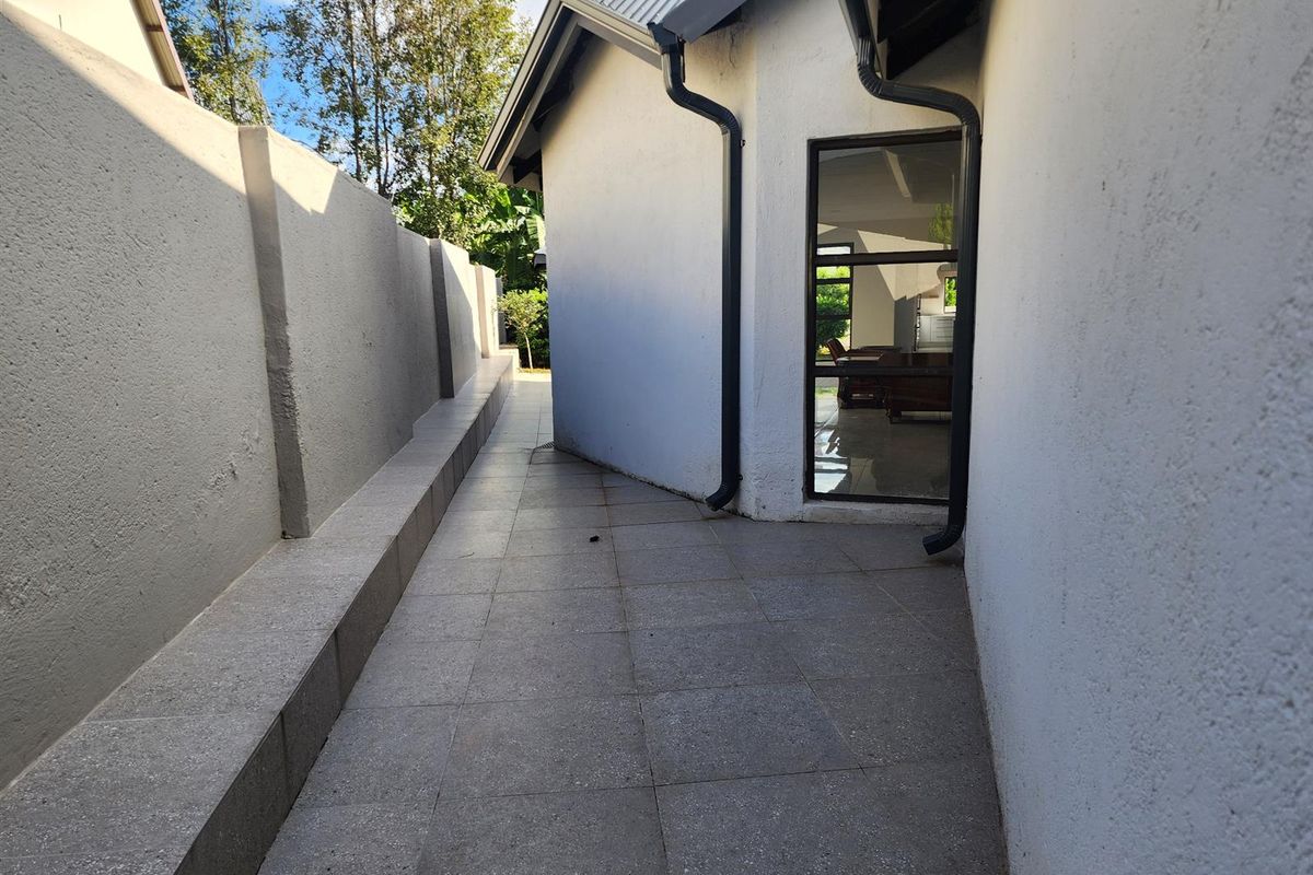 A paved side walkway or exterior passage featuring a boundary wall and direct access to the interior living space through a glass door.