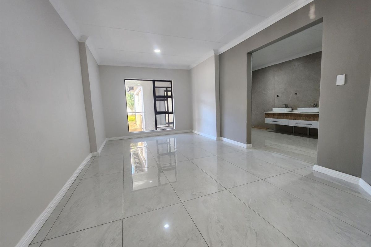 A bright, modern bedroom featuring large-format porcelain floor tiles, neutral grey walls, and an open-plan en-suite bathroom with a double vanity.